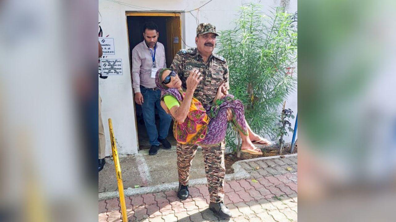 A Central Reserve Police Force (CRPF) official RN Tiwari assists a 100-year-old elderly voter as she arrives to cast her vote for the second phase of the Lok Sabha elections, at Mauganj, in Rewa on Friday. (ANI Photo) 