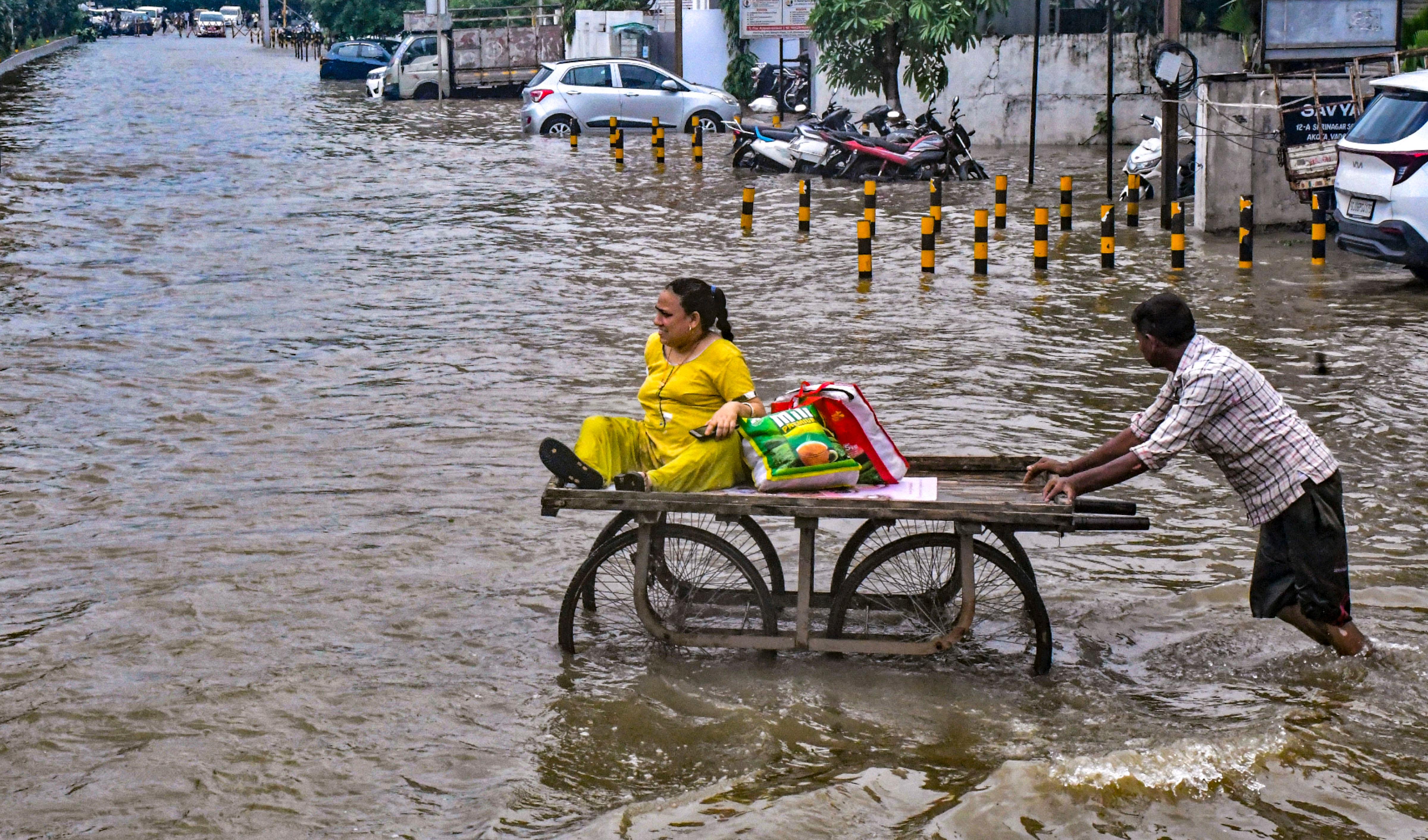 A man pushes a Vadodara resident on a cart to relocate her from a waterlogged area