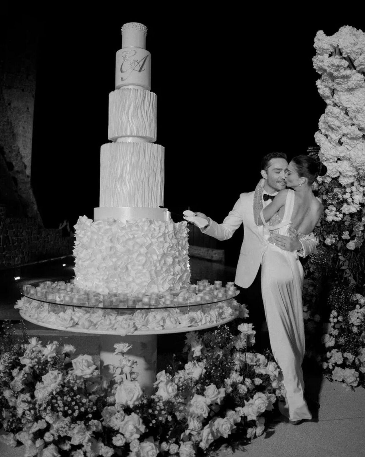 The couple pose close to their five-tiered massive wedding cake