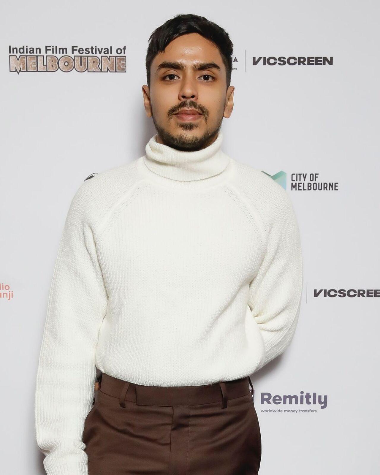 Adarsh Gourav poses on the red carpet of premiere night in a turtle neck white sweatshirt and brown pants