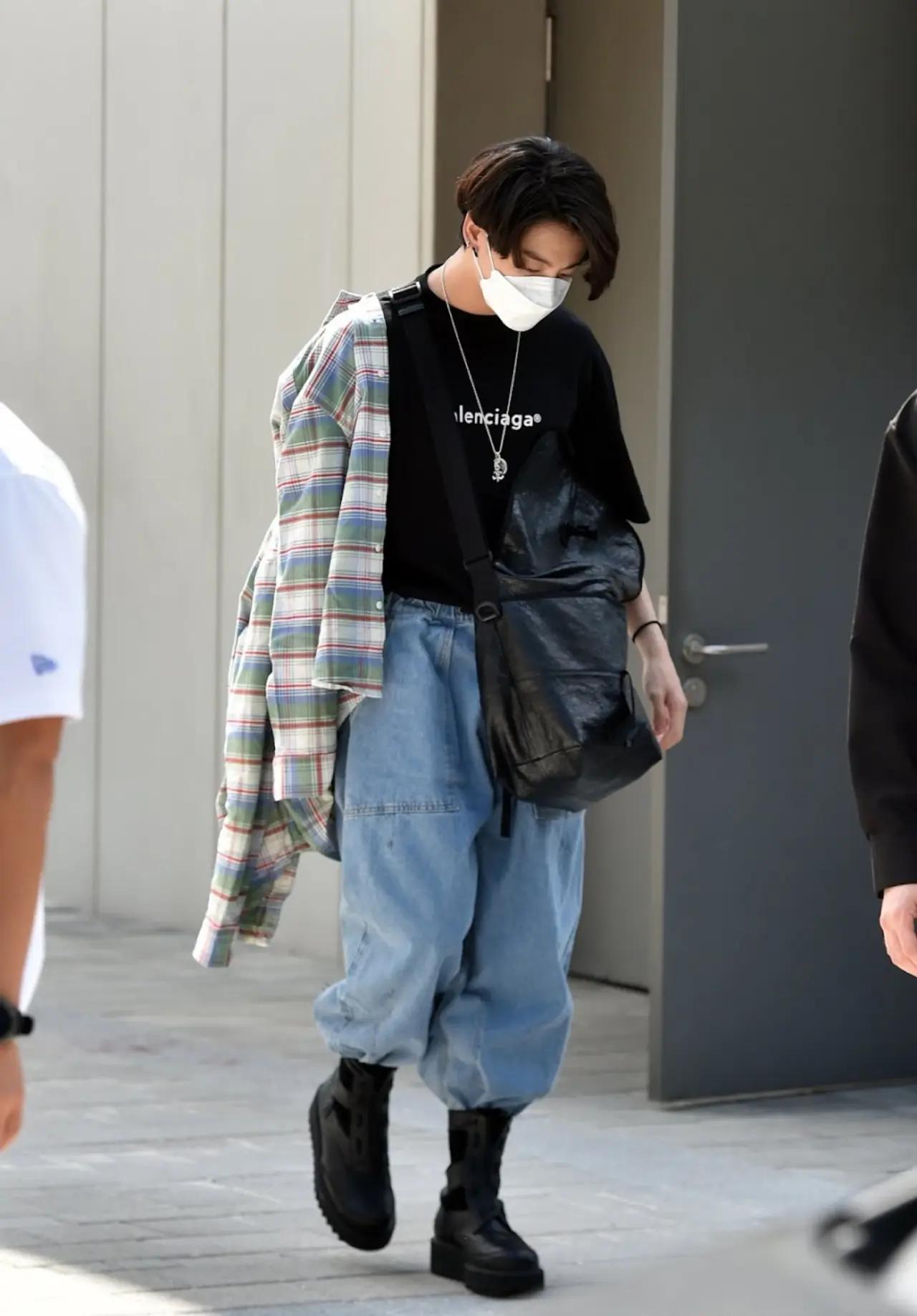 Street fashion is another essential element in Jungkook's lookbook. He often sports graphic t-shirts, hoodies, joggers, and sneakers. In this photo, he pulls off his baggy jeans and oversized flannel shirt by pairing them with more refined items like boots and a stylish leather sling bag