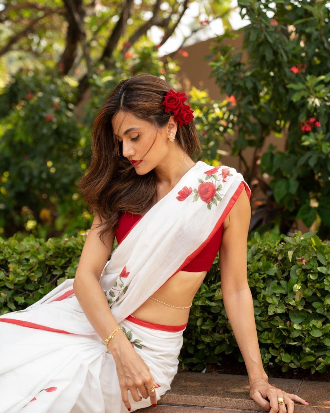 With red roses in her hair, Taapsee Pannu poses in character in this white saree with floral prints. Her accessories include a thin bracelet and a kamarbandh.
