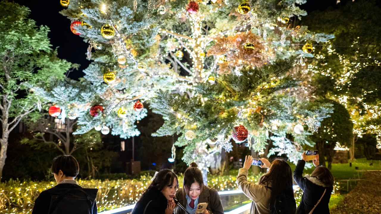 People take pictures in front of an illuminated Christmas tree at a park in Tokyo's Roppongi district