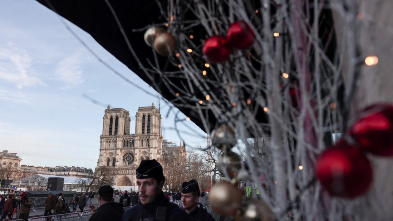 French police officers walk past Christmas decorations in front of Notre-Dame de Paris cathedral, surrounded by the security barriers and fences