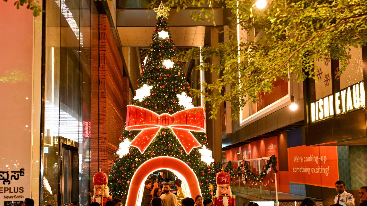 Shoppers take photographs next to a decorated Christmas tree installed in front of a store ahead of Christmas at Church Street in Bengaluru (Pic: AFP)