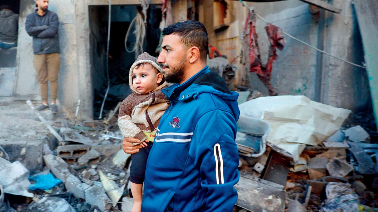 A Palestinian man carrying a child walks past a destroyed building in the Nuseirat refugee in the central Gaza Strip. Pics/AFP