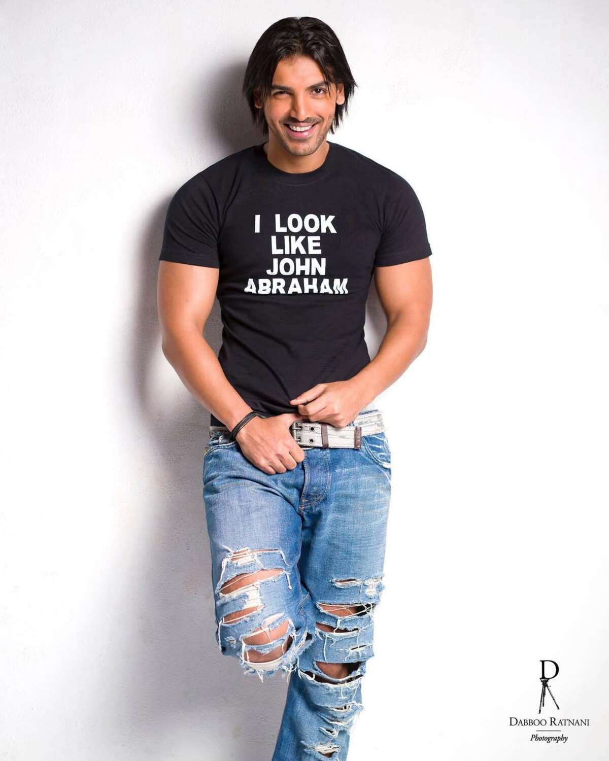John Abraham wears a dapper black tee and dons long hair with ripped blue denims. The T-shirt reads, 