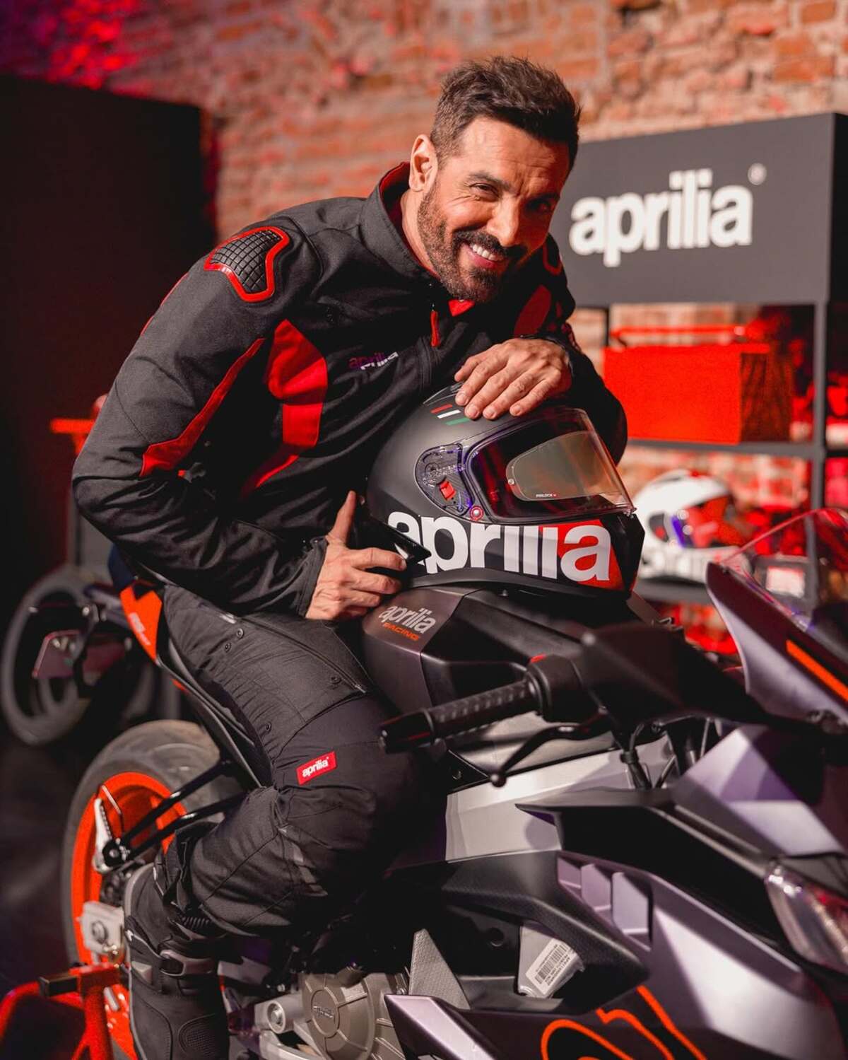 John Abraham loves biker fits and sports jerseys. He is often papped wearing jerseys of his favourite sports teams in public places. He looks charming in his red and black racing suit and protective gear. 