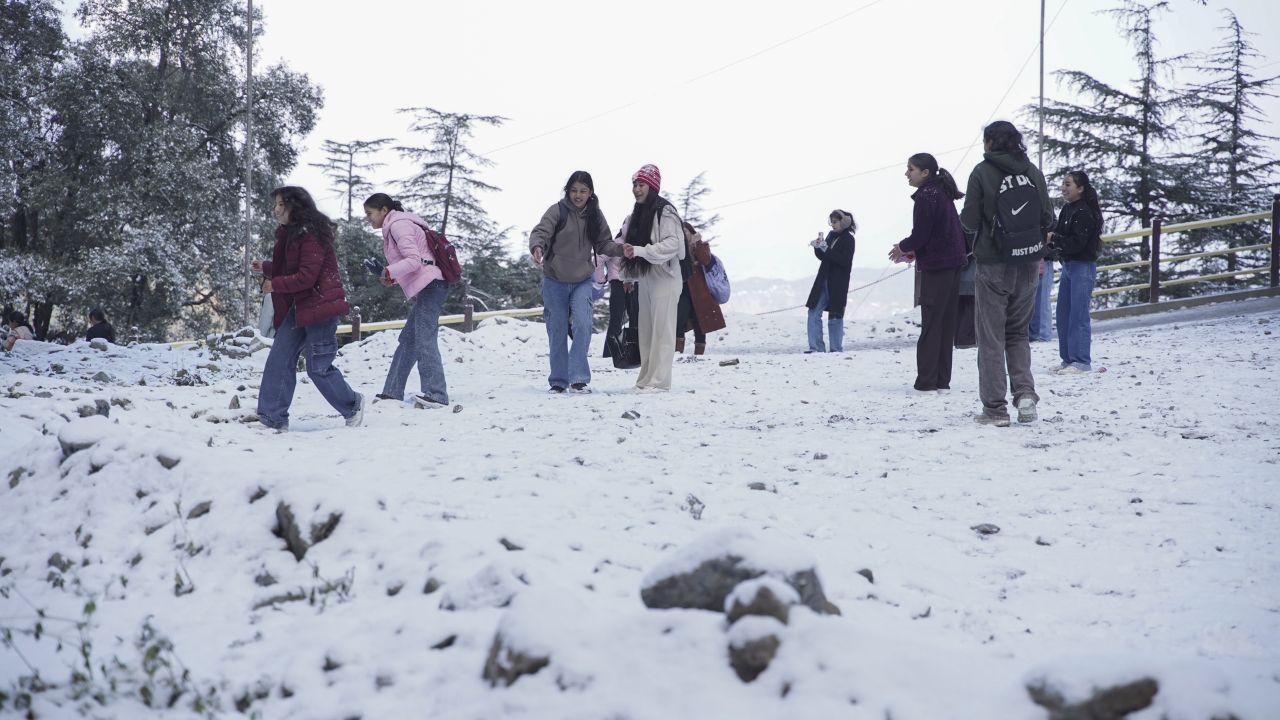 High-altitude areas and mountain passes were blanketed in snow, causing minimum temperatures to drop by four to six degrees. (In Pic: Young women visit a snow covered park after fresh snowfall in Shimla, Himachal Pradesh, Monday)