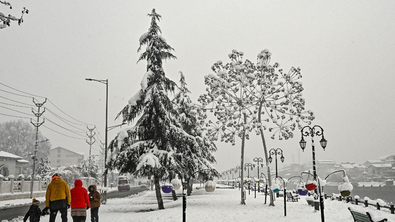 A family walks through a snow-covered road near the Jhelum River after winter's first snowfall. (Pic/ AFP)