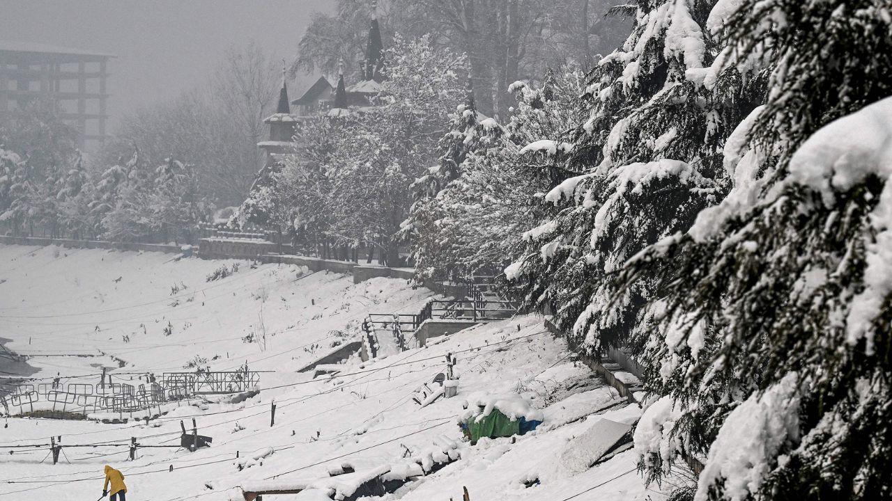 A man removes snow on the banks of river Jhelum after winter's first snowfall in Srinagar. (Pic/ AFP)