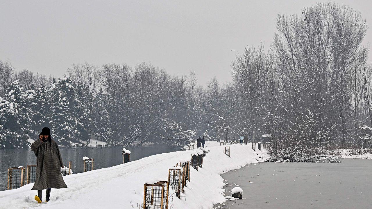 A man speaking on his mobile phone walks along the shores of forzen Dal Lake after winter's first snowfall in Srinagar. (Pic/ AFP)