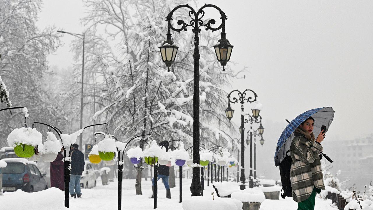 A woman holding an umbrella uses her mobile phone during winter's first snowfall in Srinagar. (Pic/ AFP)