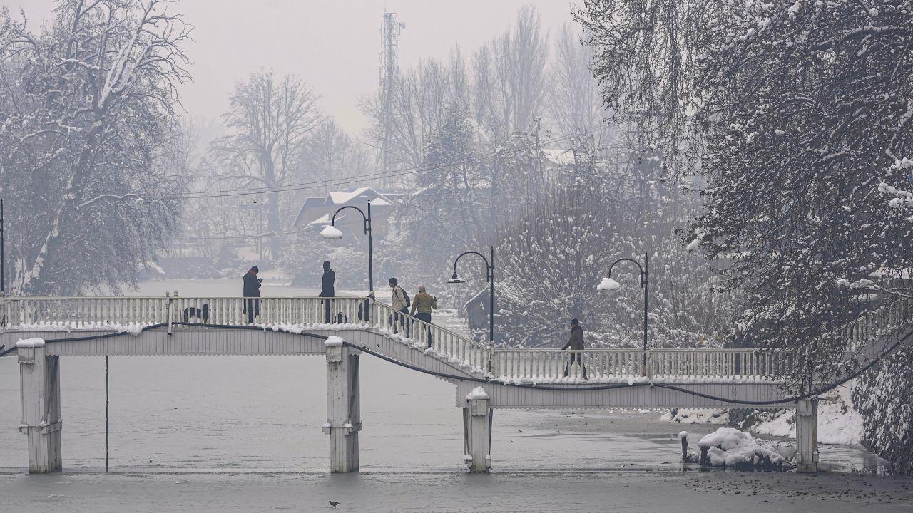 People cross a snow-covered bridge after the season's first snowfall, in Srinagar. (Pic/ PTI)