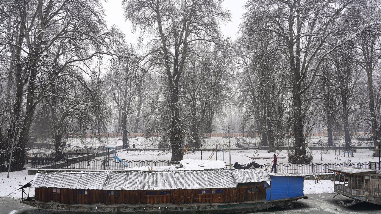 A man clears snow atop a houseboat after the season's first snowfall, in Srinagar. (Pic/ PTI)