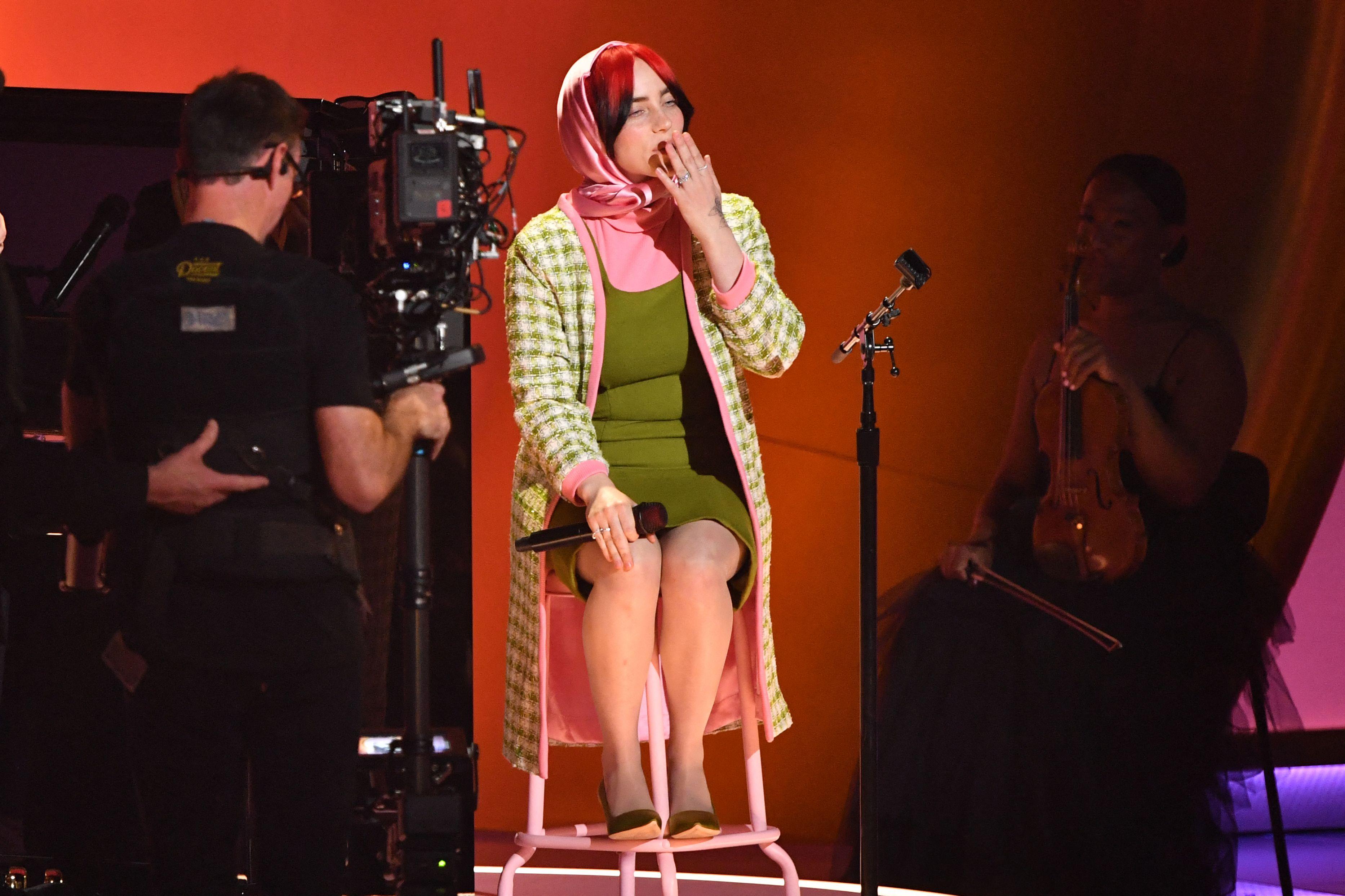 Before her big win at the ceremony, Billie Eilish also performed her song 'What Was I Made For?' The pop star fittingly looked like a vintage Barbie doll during her set -- wearing a '60s-inspired green dress and matching jacket, which was embellished in pink to perfectly match the satin pink scarf wrapped in her hair, 