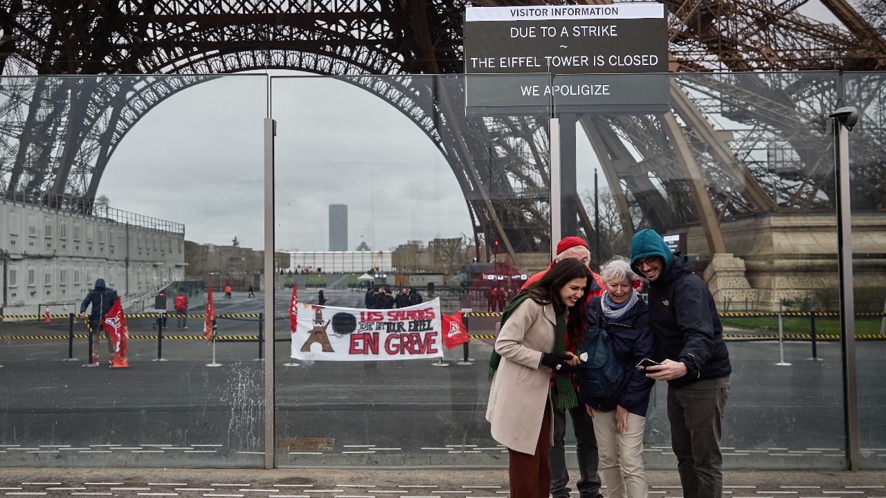 Pedestrians take a picture next to the Eiffel Tower, and a board (Top R) informing visitors that the monument is closed as staff go on strike, and a displayed banner (C) reading 