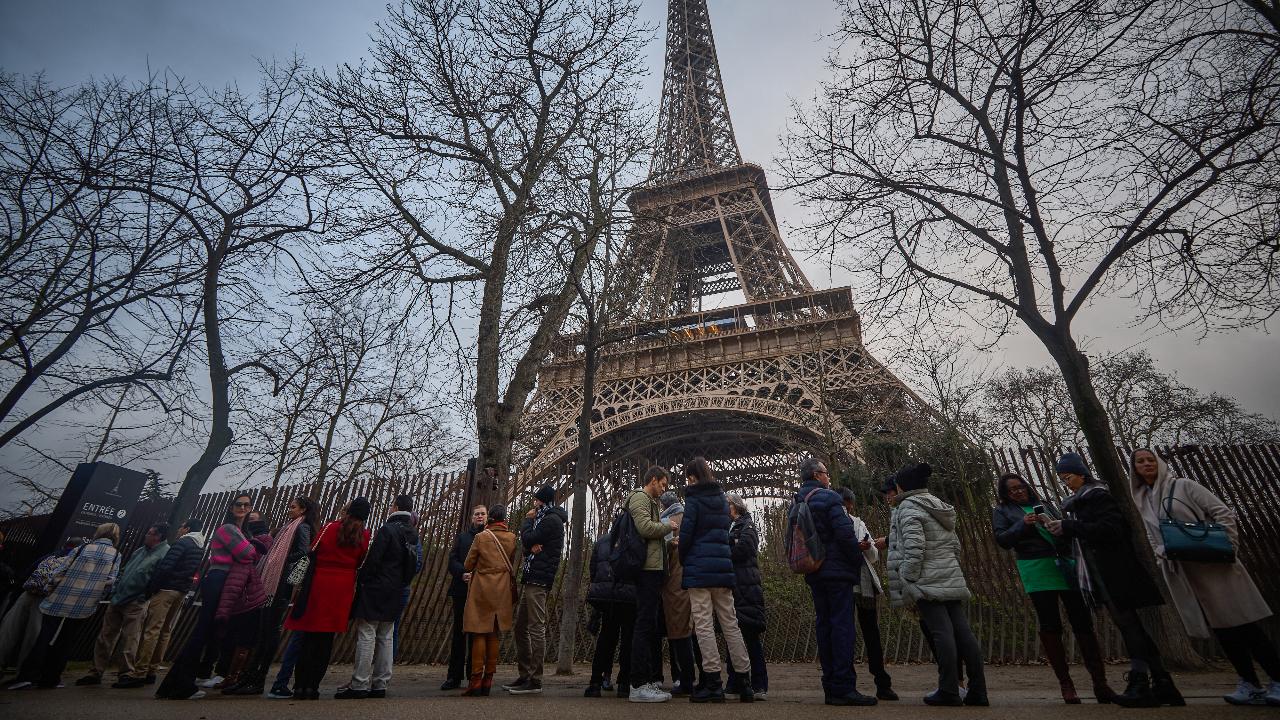 Tourists walk next to the Eiffel Tower at sunrise as the monument is shut due to a staff strike over the financial management of the monument by the city, closing the monument to the public during the second week of the French school holidays, in Paris on February 19.