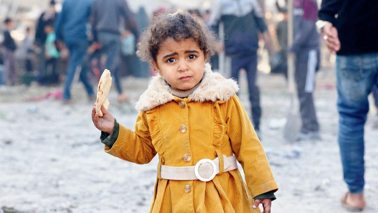 A girl eats bread as people check debris in Rafah