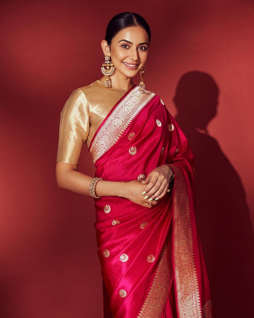 In this captivating look, the actress dons a stunning red saree adorned with intricate golden embroidery. The saree is elegantly paired with a matching blouse, and Rakul completes the look with a chic bun hairstyle