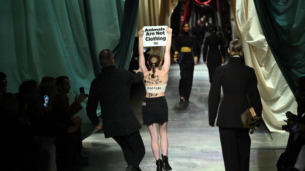 A security guard runs to stop a woman holding a poster reading 'animals are not clothing' during the Fendi collection show