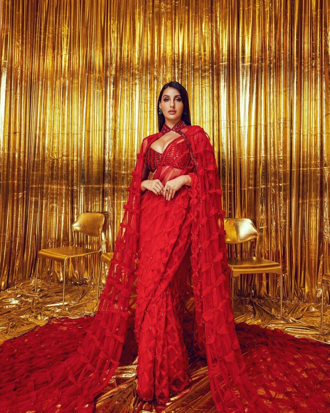 Nora Fatehi looks magnificent in this red saree created by Manish Malhotra that comes with an elaborate cape