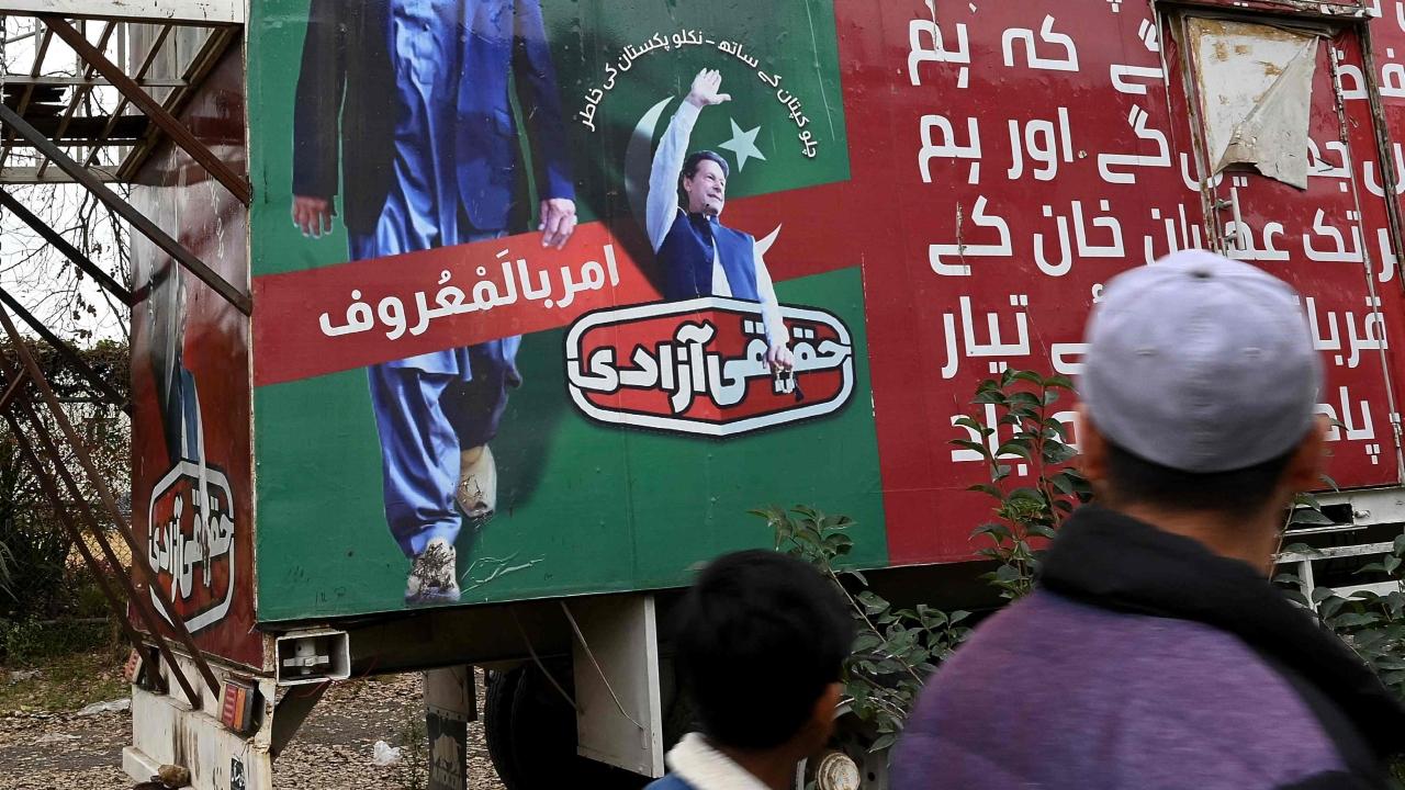 People walk past a poster of jailed Pakistan's former Prime Minister Imran Khan, near his party office in Islamabad. The former international cricket star has been given three lengthy prison sentences in under a week and been banned from politics for 10 years