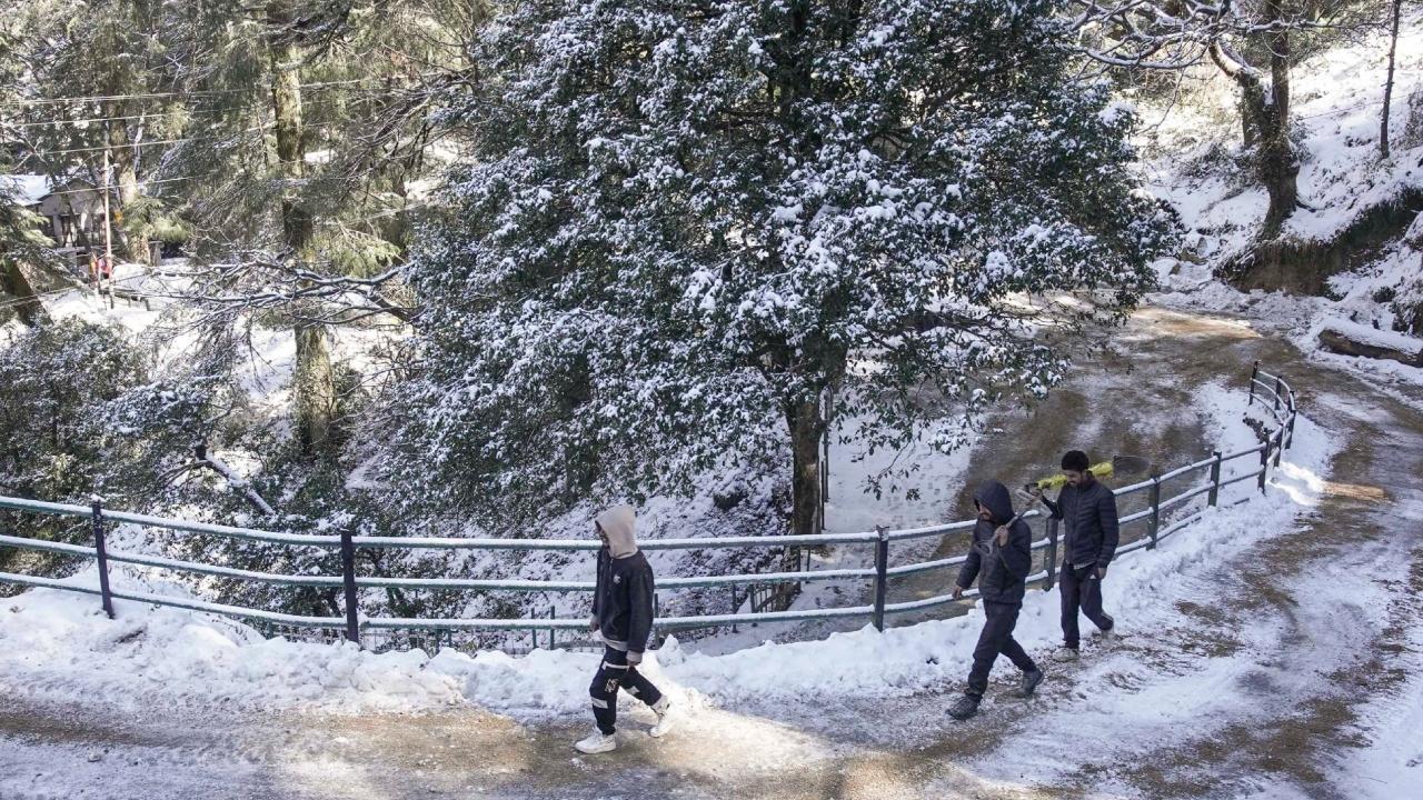 Workers are seen on a road partially covered in snow after fresh snowfall in Shimla on Saturday