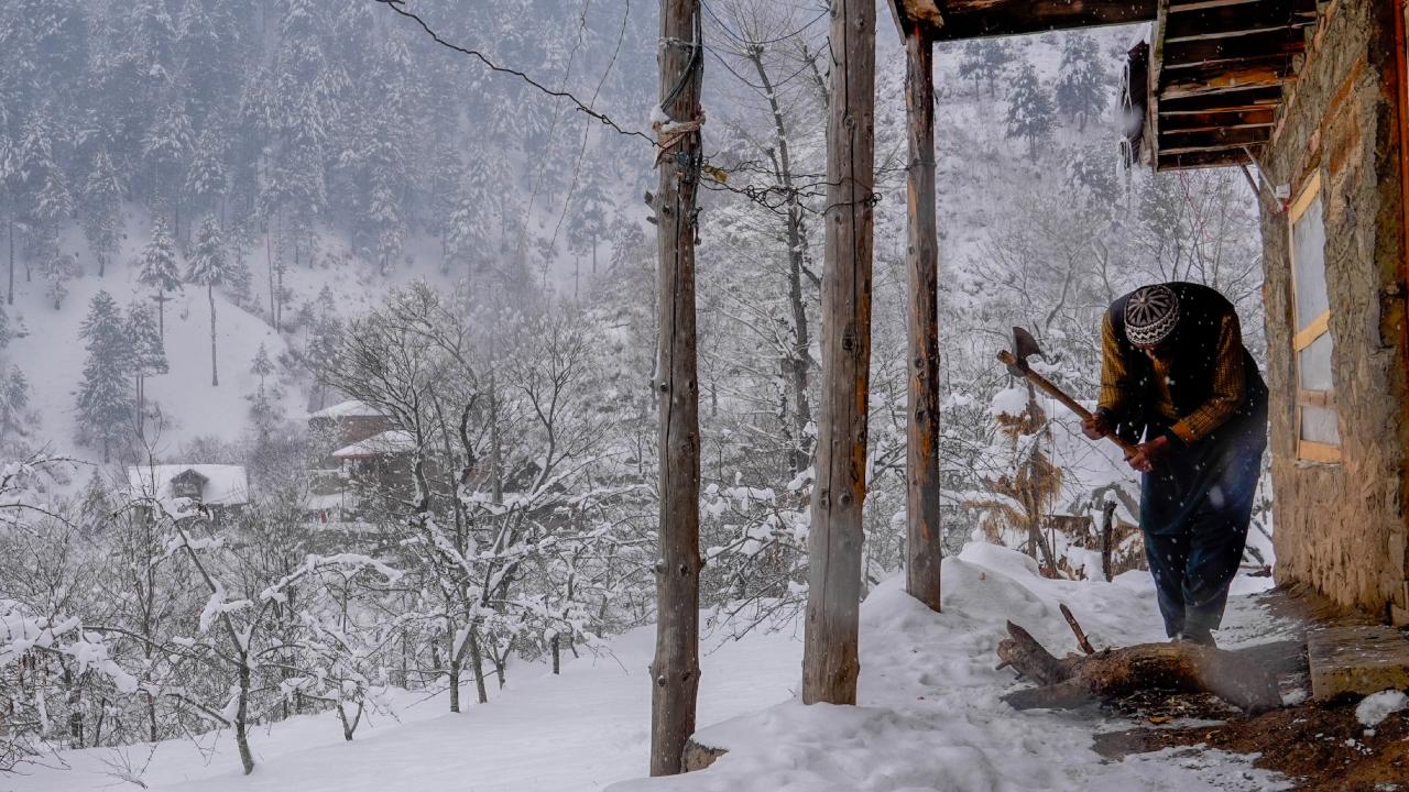A man chops a log of wood outside his house during snowfall, on the outskirts of Srinagar on Saturday