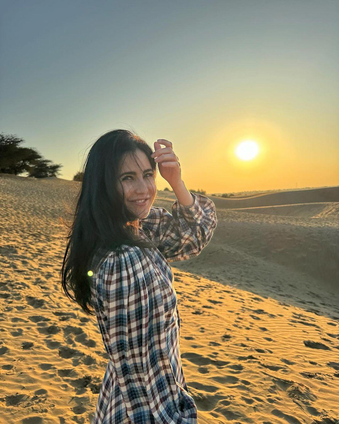 In this picture, Katrina wears a stunning checkered dress and poses in front of the setting sun in the desert