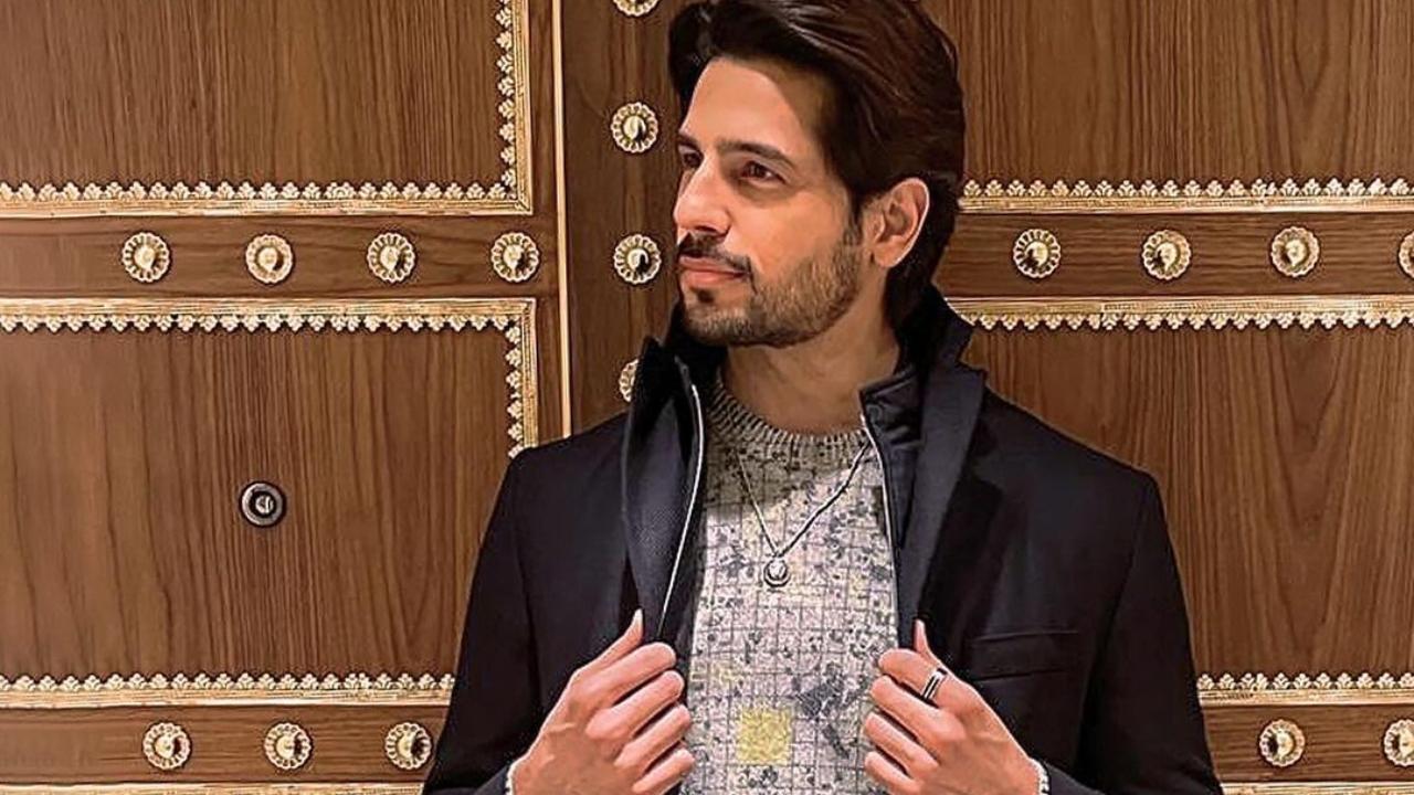 Sidharth dressed for the occasion in a patterned gray sweater, black slacks, and a black over coat