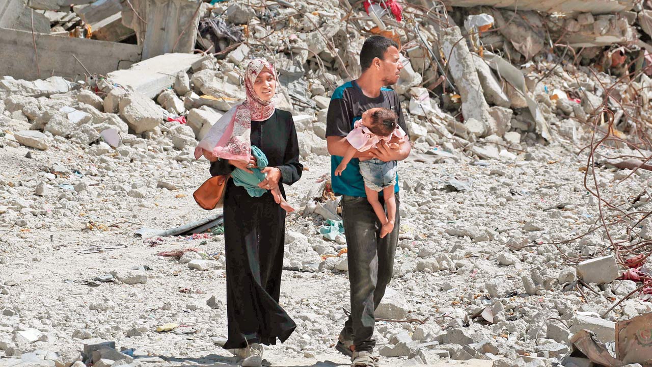 A Palestinian couple holds their children as they walk through debris in Khan Yunis. Pic/AFP