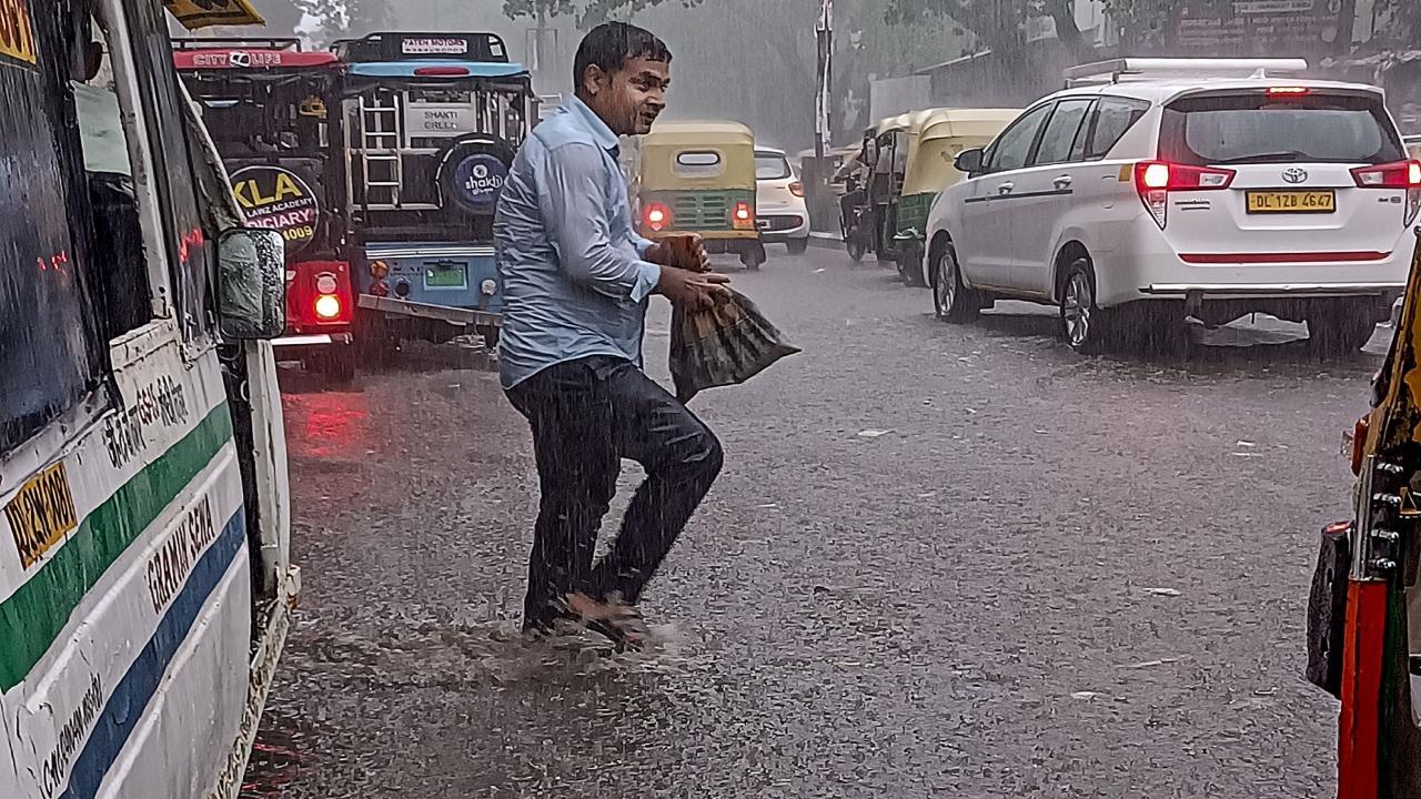 A man crosses a waterlogged road amid rains, at Mukherjee Nagar in New Delhi. Pics/PTI