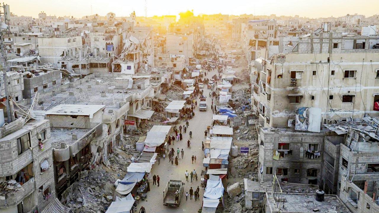 Palestinians walk through a street market in Khan Younis, amid destroyed buildings