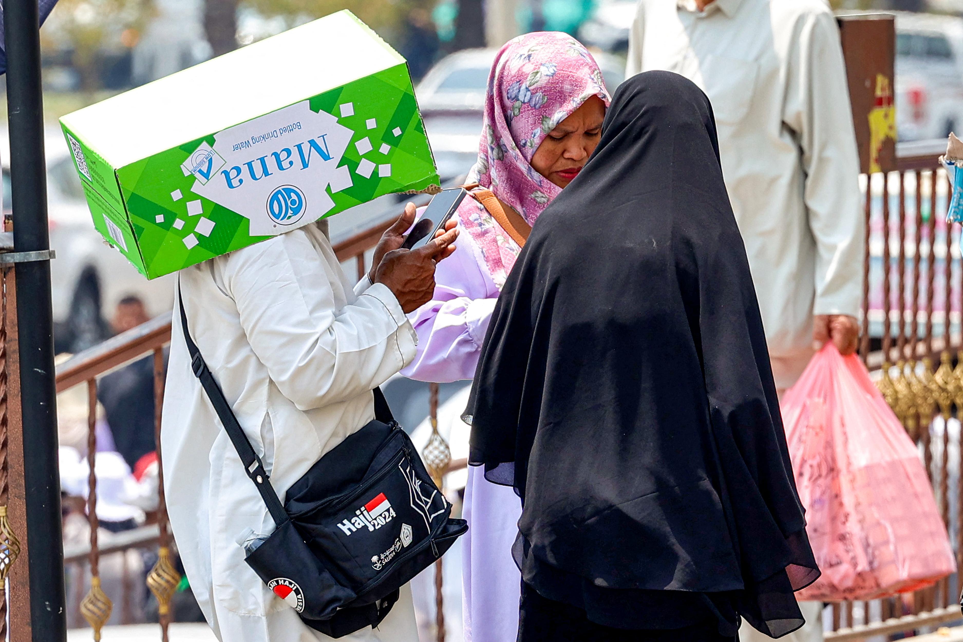 A man shades his head with a cardboard box as he browses his phone while standing next to other women in Saudi Arabia's holy city of Mecca on June 20.