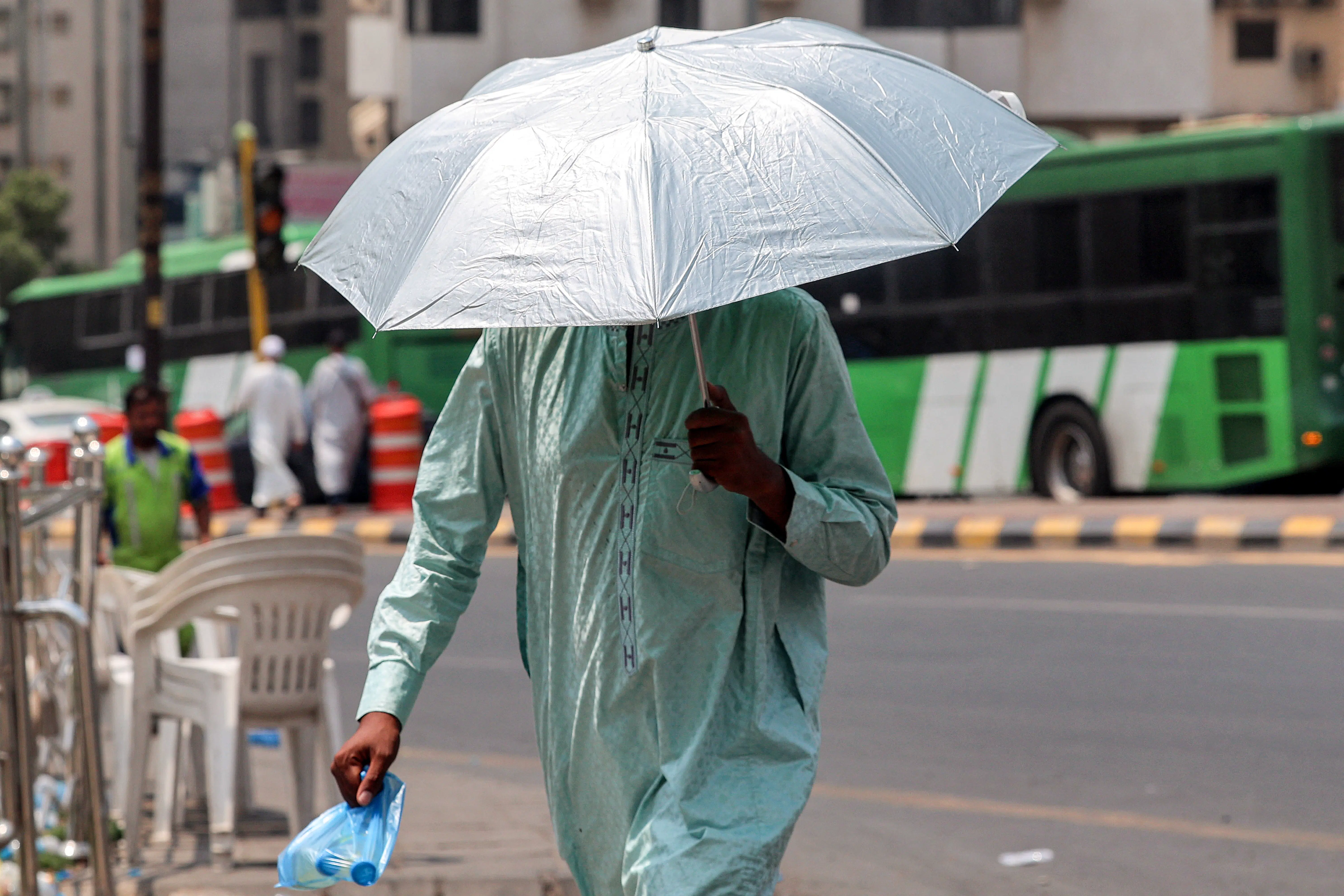 A man shades himself with an umbrella as he walks with a bag of water bottles in Saudi Arabia's holy city of Mecca.