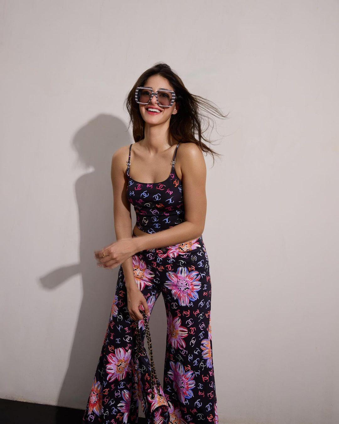 She paired a printed spaghetti strap top with matching print pants, a printed bag, and large sunglasses.