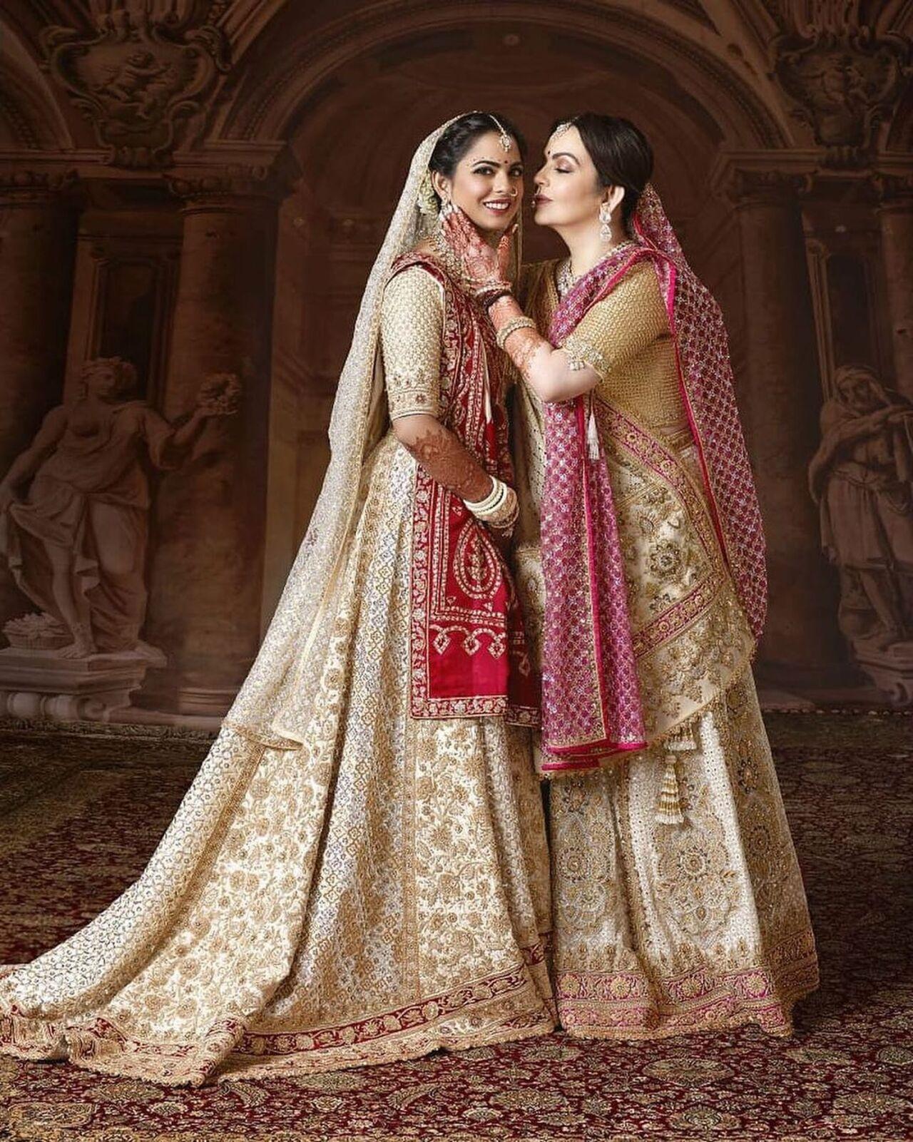Isha Ambani Piramal wore a 16-paneled ghagra in 2 shades of off-white that featured a trail. Each panel was hand embroidered. Vermilion, the iconic bridal hue featured in the zardozi borders, lends auspiciousness to the ensemble. She layered it with her mother’s 35-year-old wedding sari. 