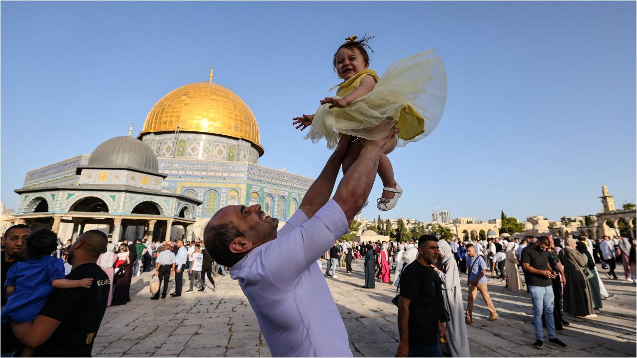 A man lifts a child as Palestinian Muslims convene at the Al-Aqsa mosques compound in Jerusalem, with the Dome of the Rock in the background