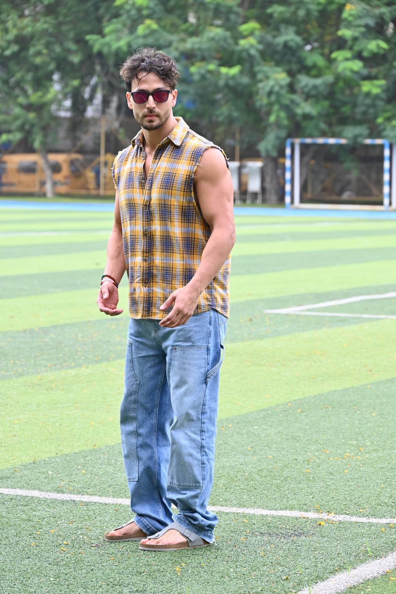 Tiger Shroff flexed his muscles as he was photographed on a football turf. He wore a sleeveless flannel shirt and a pair of baggy jeans. 