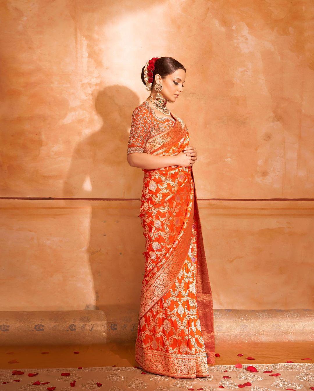 Kangana just glows in orange. In this look, Kangana wore an embroidered orange saree and paired it with a matching blouse. The actress tied her hair in a chic bun and elevated it with white mogra and red roses