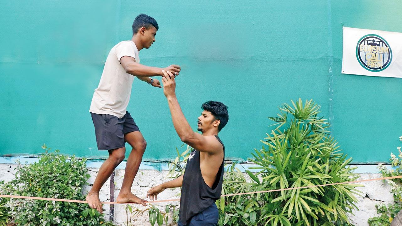 A calisthenics trainer helps a participant with his balance on the rope