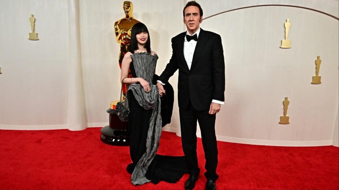 Couple Riko Shibata and Nicolas Cage posed together wearing coordinated black outfits. Cage sported a classic black tuxedo, while Shibata walked the red carpet in a black and grey structured gown. 