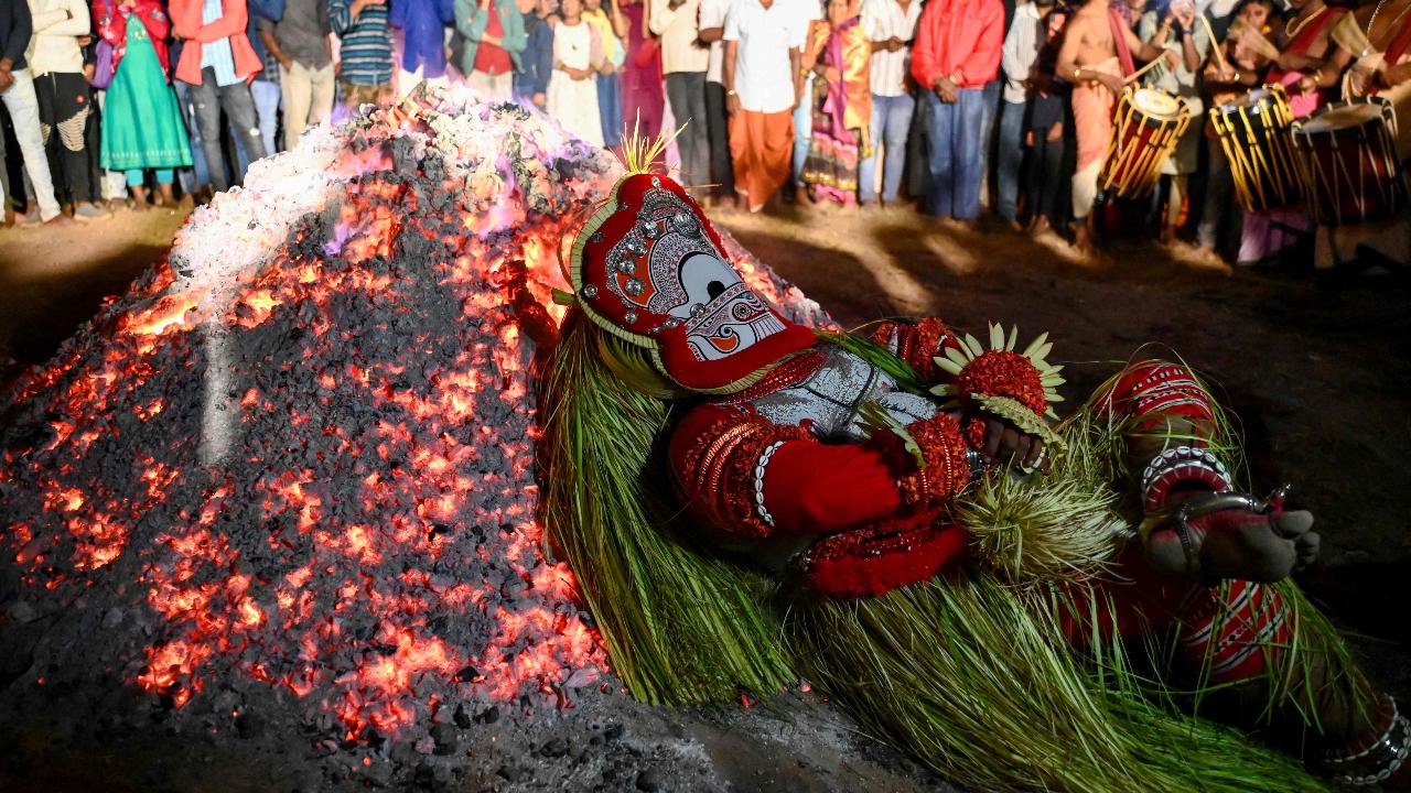 An Indian artist dressed as the Hindu deity Pottan lies on burning cinders of coal during the festival