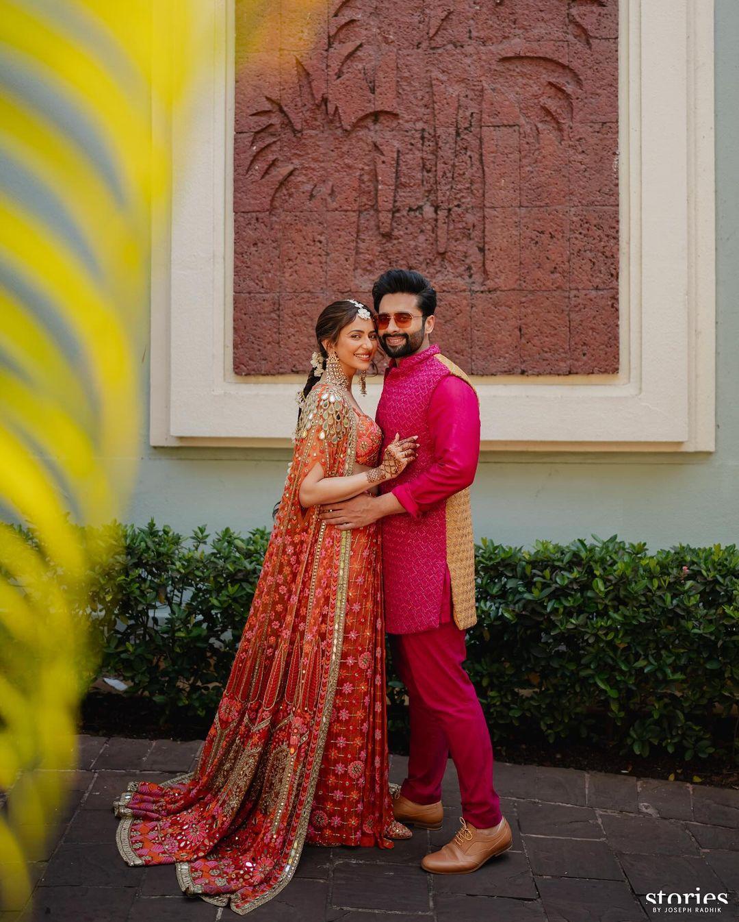 Clad in a bespoke phulkari lehenga by Arpita Mehta in the shade of rust. Paired with a long cape with intricate embroidery, Rakul Preet Singh accessorised her Mehendi look with giant pair of earrings and a maang tika. Jackky Bhagnani on the other hand wore a hot pink sherwani set
