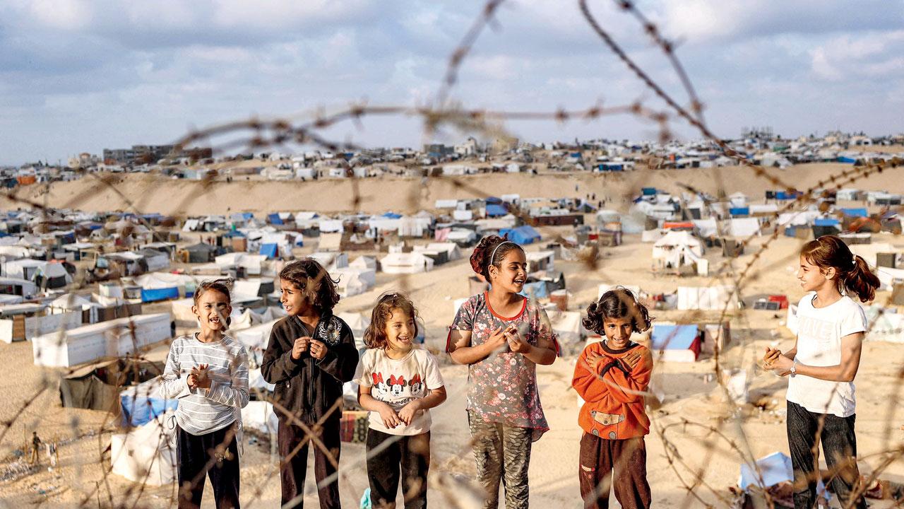 Children stand behind barbed-wire along a slope near a camp housing displaced Palestinians in Rafah. Pic/AFP