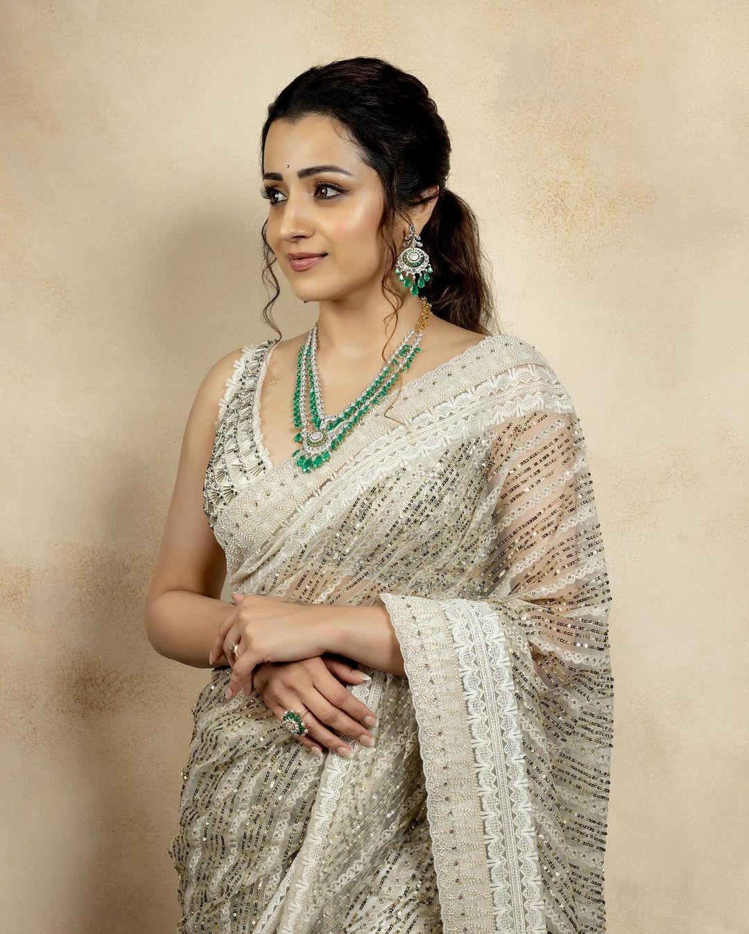 In this look, Trisha wore a stunning sheer beige saree with a heavy border and strappy blouse. To add some colour to her look, she added a green jewellery set