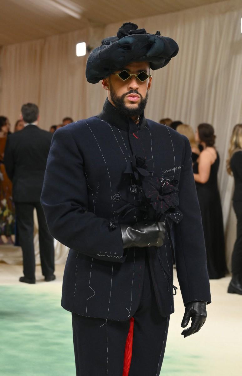 Bad Bunny chose to wear a custom outfit from the Maison Margiela Artisanal Collection by John Galliano. His attire featured a black satin corset, a navy wool smoking jacket with black lapels made of grosgrain, and a unique hat made of blue foam covered in blue stocking material.