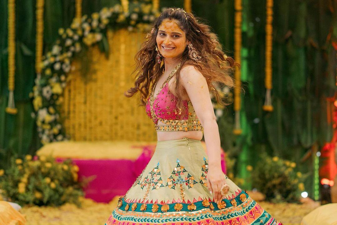 At her Haldi ceremony, Arti donned a pink choli paired with a green mid-length lehenga skirt. 