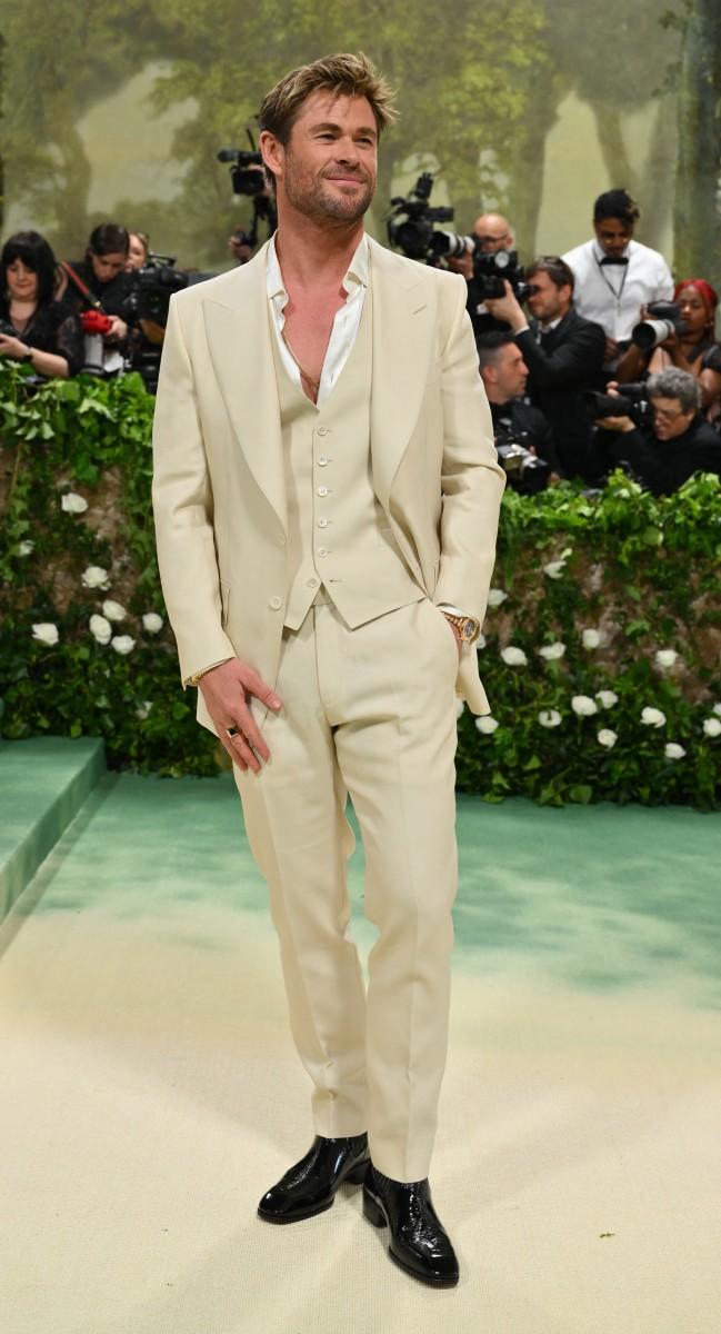 At the 2024 Met Gala, Chris Hemsworth rocked a tailored cream wool three-piece suit paired with sleek black patent leather boots. His hair had a casual tousled look, and he accessorized with a rose gold Chopard watch on his wrist.